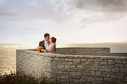 Bride and Groom kiss behind a short brick wall over looking the ocean